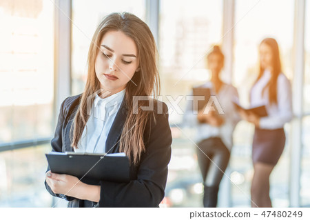 Beautiful brunette business woman in white suit with folder of documents in her hands outdoors. copy Beautiful brunette business woman in white suit with folder of documents in her hands outdoors. copy 47480249