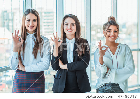 Young pretty business girls show a good gesture. Dressed in classic clothes, smiling copy space Young pretty business girls show a good gesture. Dressed in classic clothes, smiling copy space 47480388