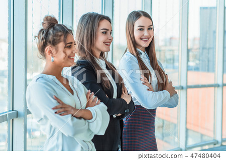 With pleasure, three business women cross their arms, looking at the camera. With pleasure, three business women cross their arms, looking at the camera. 47480404