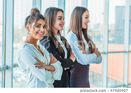 With pleasure, three business women cross their arms, looking at the camera. With pleasure, three business women cross their arms, looking at the camera. 47480407