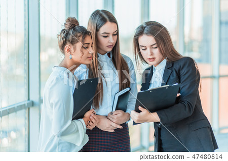 Group of friendly three multiethnic business people stand in office hall, hold papers, study Group of friendly three multiethnic business people stand in office hall, hold papers, study 47480814