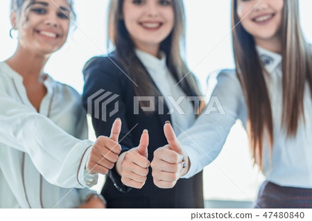 Three young business girls in the office. Dressed in classic clothing style, showing thumbs up Three young business girls in the office. Dressed in classic clothing style, showing thumbs up 47480840