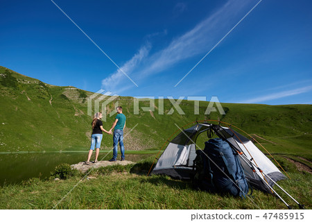 Rear view of cute pair stand near camping against mighty green mountain Rear view of cute pair stand near camping against mighty green mountain 47485915