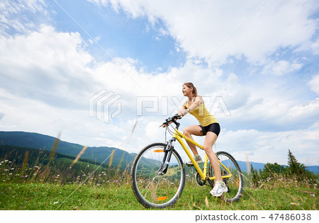 Attractive female cyclist with yellow mountain bicycle, enjoying sunny day in the mountains 47486038