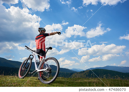 Back view of male athletic professional biker standing with cross country bicycle on top of hill 47486070