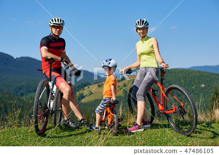 Young modern family tourists bikers, mom, dad and child resting on bikes looking in camera 47486105