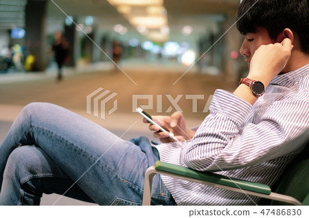 Young man enjoy using smart phone while waiting Young man enjoy using smart phone while waiting 47486830