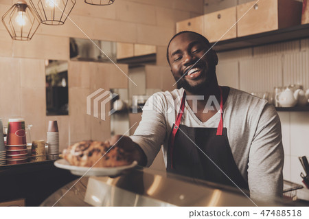 Male barista serves a croissant ordered to client Male barista serves a croissant ordered to client 47488518