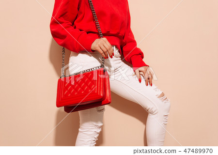 Fashion young woman in white jeans and sweater with red bag clutch in hands near street wall 47489970