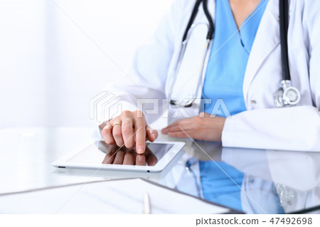 Woman doctor using tablet computer while sitting at the desk in hospital office, closeup. Healthcare Woman doctor using tablet computer while sitting at the desk in hospital office, closeup. Healthcare 47492698