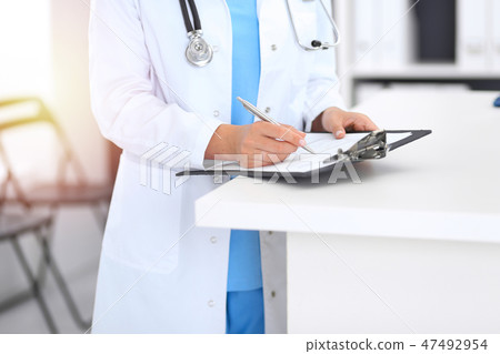 Unknown doctor woman at work, hands close-up. Female physician filling up medical form while Unknown doctor woman at work, hands close-up. Female physician filling up medical form while 47492954