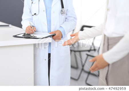 Unknown doctor and female patient discussing something while standing near reception desk in Unknown doctor and female patient discussing something while standing near reception desk in 47492959
