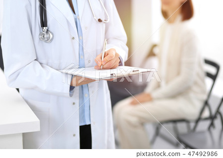 Doctor woman filling up medical form while standing near reception desk at clinic or emergency 47492986