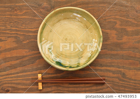 A dish made of earth and chopsticks placed on a brown table 47493953