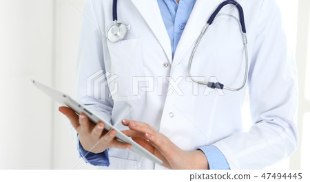 Woman doctor using tablet computer while standing straight in hospital closeup. Healthcare 47494445