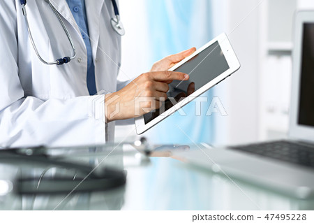 Woman doctor using tablet computer while sitting. Reflecting glass table is a working place of 47495228