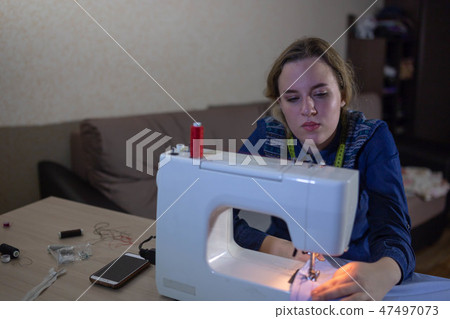 A young girl seamstress works at home sewing machine. Works at night A young girl seamstress works at home sewing machine. Works at night 47497073