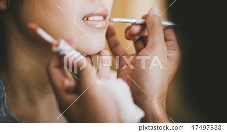 Make-up stylist brushing lipstick on young woman Make-up stylist brushing lipstick on young woman 47497888