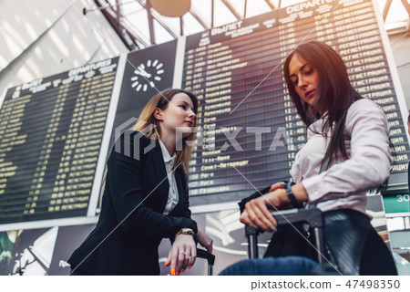 Two female tourists standing near flight information display in international airport Two female tourists standing near flight information display in international airport 47498350