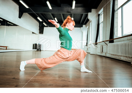 Beautiful slim yoga coach in a green turtleneck doing balancing asana Beautiful slim yoga coach in a green turtleneck doing balancing asana 47500054