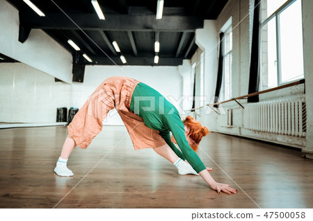 Beautiful slim yoga coach in a green turtleneck stretching her back 47500058