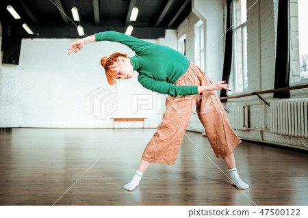 Pleasant-looking fit yoga instructor in a green turtleneck standing in asana Pleasant-looking fit yoga instructor in a green turtleneck standing in asana 47500122