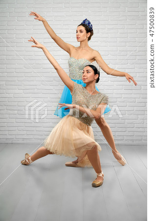 Ballerinas in beige and blue dresses looking above in studio Ballerinas in beige and blue dresses looking above in studio 47500839