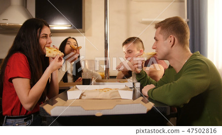 Company of young friends sitting in kitchen and eating pizza from the delivery box 47502816