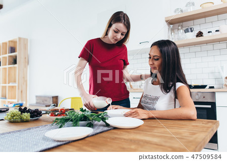 Woman pour milk into bowl her friend in kitchen 47509584