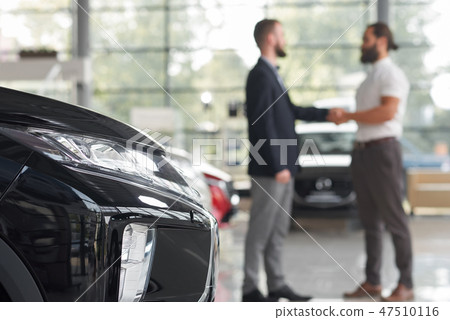 Car dealer shaking hands with client in car showroom. Car dealer shaking hands with client in car showroom. 47510116