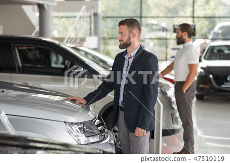 Men observing automobiles in showroom. 47510119