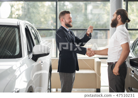 Car dealer giving keys to customer, shaking hands. 47510231