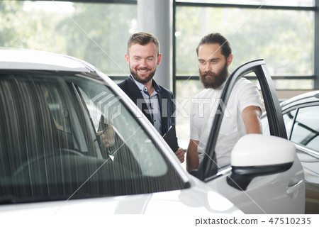 Client of car dealership observing car with manager. 47510235