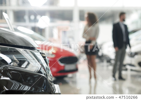 Car headlight and people observing automobiles in showroom. 47510266