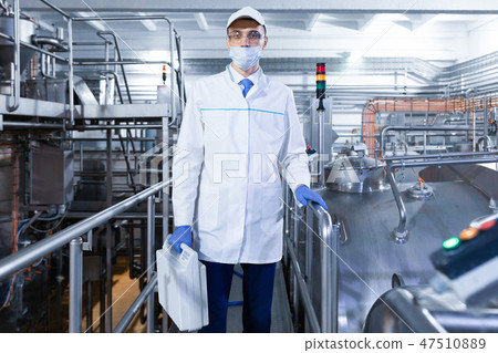 man in mask and robe with a briefcase in hand standing on a Factory dairy products man in mask and robe with a briefcase in hand standing on a Factory dairy products 47510889