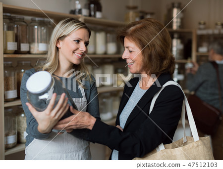 A female shop assistant serving a senior customer in a zero-waste shop. A female shop assistant serving a senior customer in a zero-waste shop. 47512103