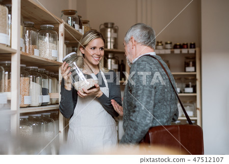 Young female shop assistant serving a senior man in a zero waste shop. 47512107