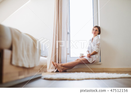 A young woman with night shirt sitting by the window in the morning. A young woman with night shirt sitting by the window in the morning. 47512156