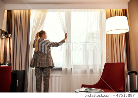 Businesswoman in dark hotel room opens curtains on window to the morning light 47513897