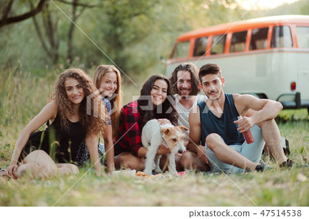 A group of young friends with a dog sitting on grass on a roadtrip through countryside. A group of young friends with a dog sitting on grass on a roadtrip through countryside. 47514538