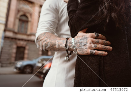 The man's hand in tattoos and jewelry embraces a girl's waist. The man's hand in tattoos and jewelry embraces a girl's waist. 47515972
