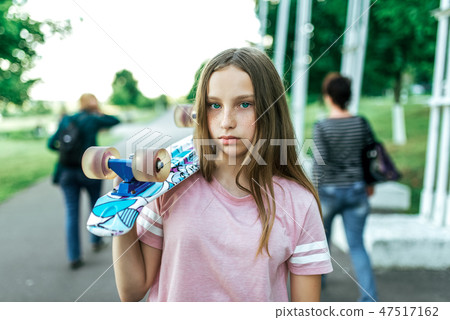 Teenager girl in the summer in city, sad stands in the park, upset, holding a skateboard on her Teenager girl in the summer in city, sad stands in the park, upset, holding a skateboard on her 47517162