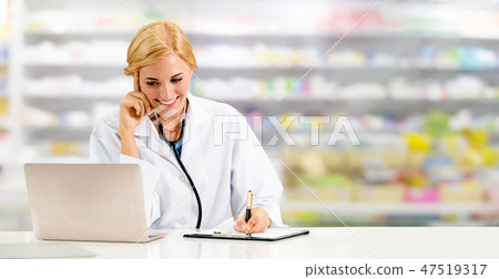 Pharmacist using laptop computer at pharmacy. 47519317