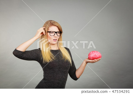 Woman in eyeglasses being confused holding brain 47534291