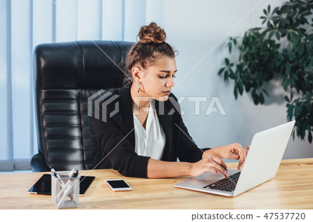 A young girl dressed in business clothes is working on a laptop. 47537720