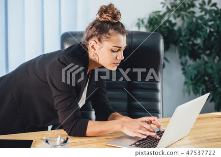 A young girl dressed in business clothes is working on a laptop. 47537722