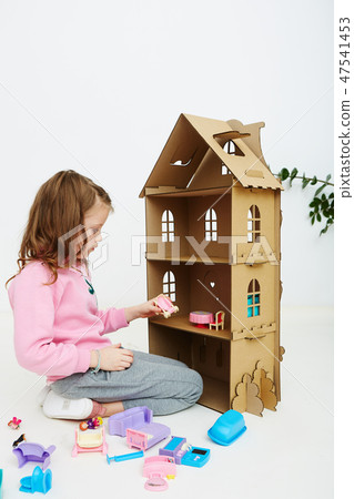 Happy girl plays with doll house and doll house furniture. Funny lovely child is having fun. 47541453