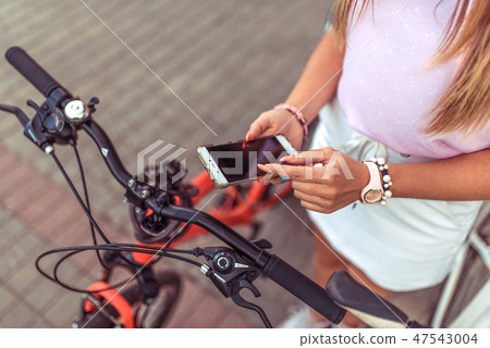 Woman girl standing in park by bike. In summer, in city, in hand of a smartphone, application 47543004