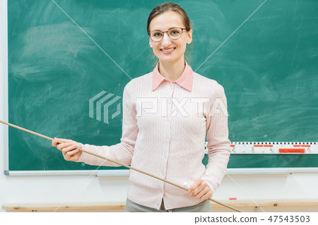 Friendly teacher standing in front of blackboard in class 47543503