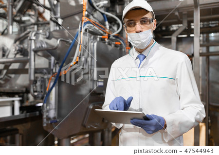 man in a mask and a Bathrobe stands with a tablet in his hands at the dairy Plant 47544943